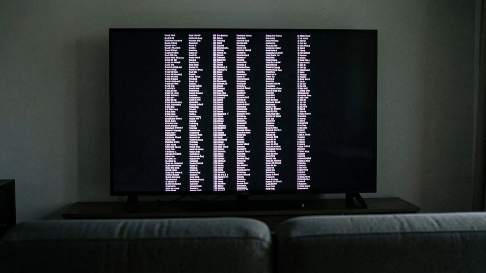 A television in a dark room showing scrolling end credits in long columns of small pale text