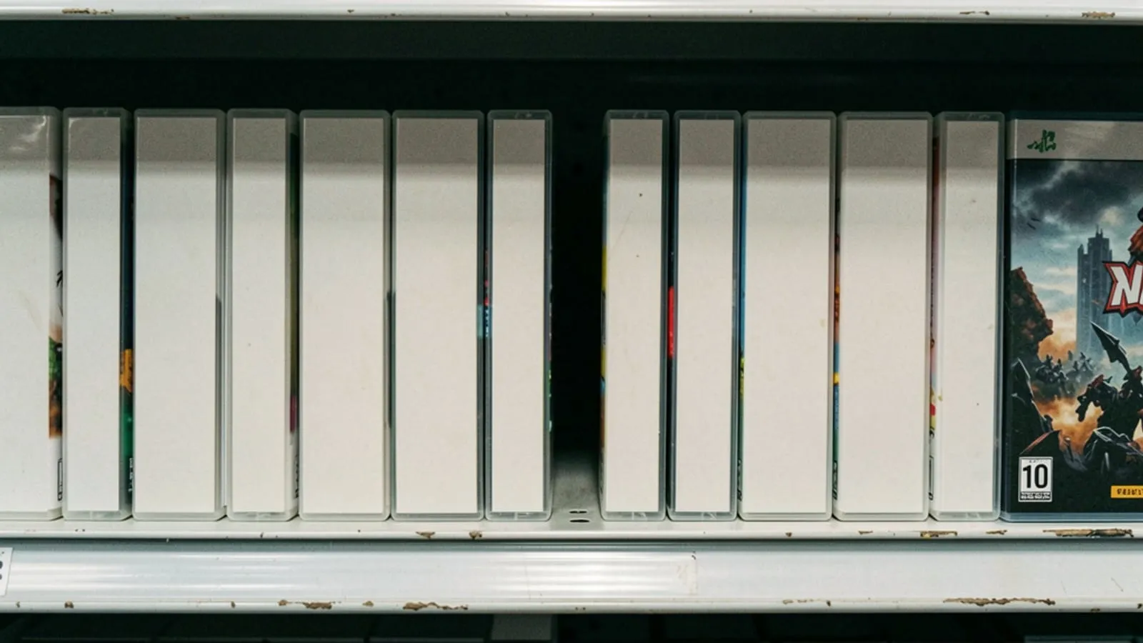 A retail shelf of plain boxed console games photographed straight on, one gap where a case has been removed