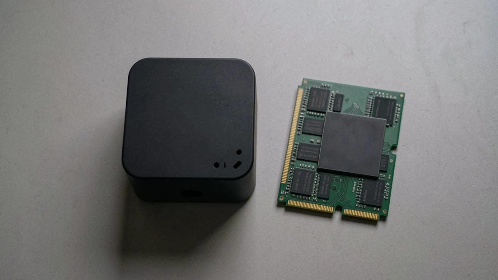 A small matte black cube PC on a desk beside a stack of green memory modules and a dark silicon package